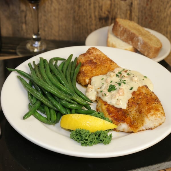 Pan-seared fish with creamy sauce, green beans, lemon, and bread on a rustic table.