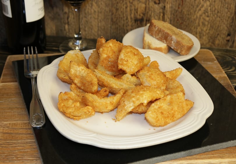 A plate of golden-brown fried calamari, a fork, bread, and a glass of red wine.