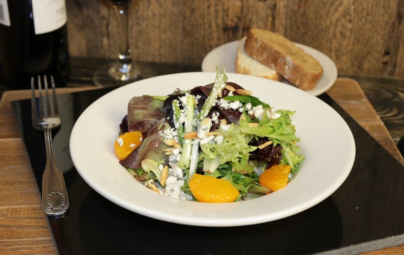 A vibrant salad with mixed greens, mandarin oranges, blue cheese, and almonds, served with bread and wine.